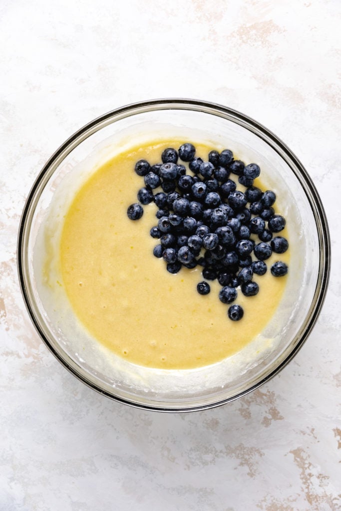 Blueberries poured on top of a bowl of bread batter.