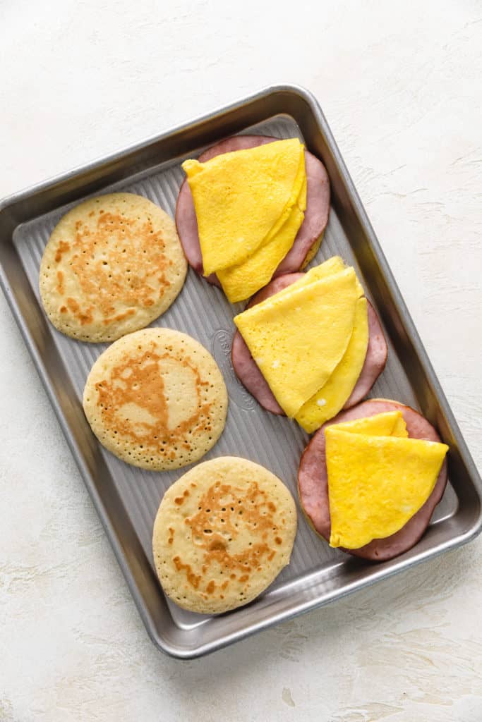 Eggs being added to breakfast sandwiches.