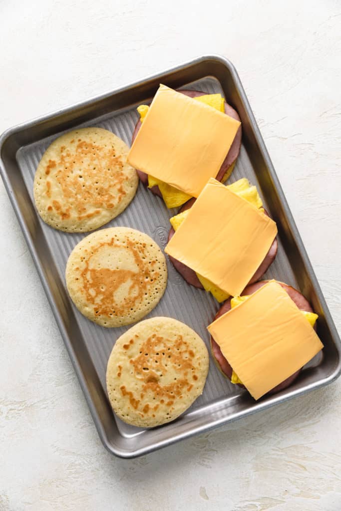 Top down view of cheese being added to breakfast sandwiches.