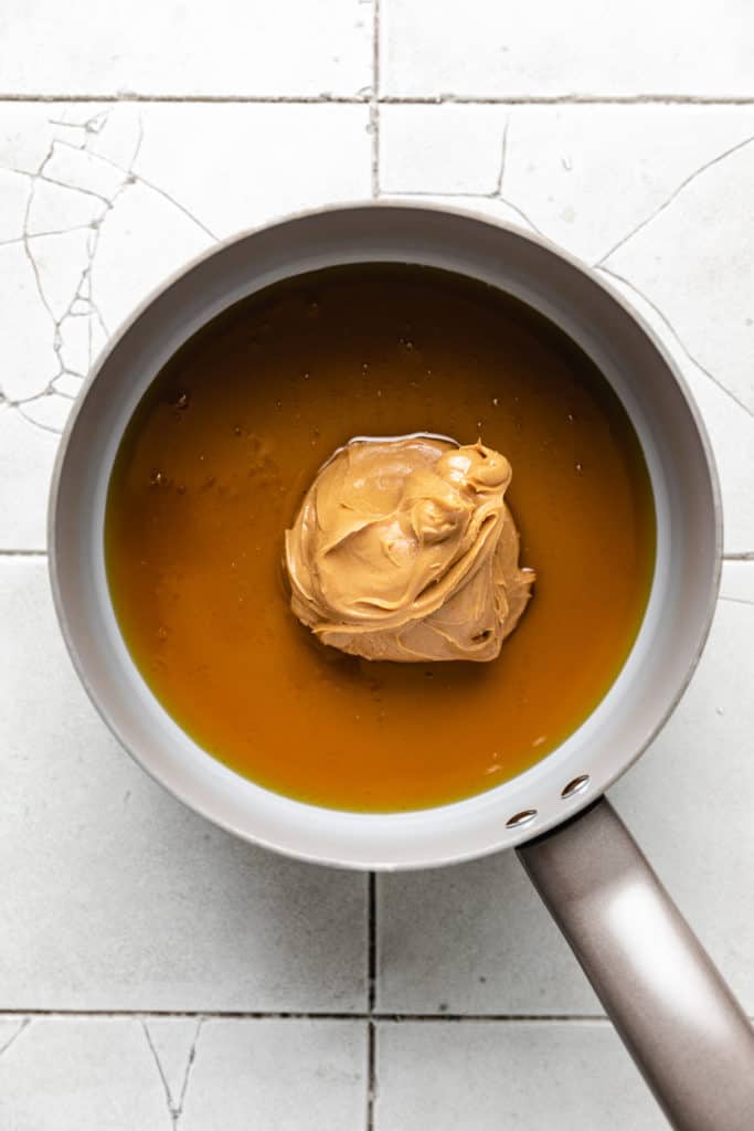 Spoon of peanut butter dropped into a pan of honey.