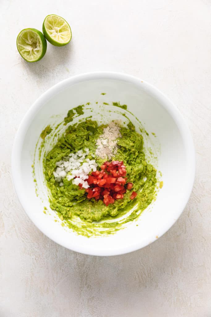 Avocados, tomatoes, onions, and seasonings in a white bowl.