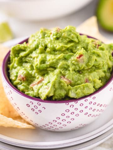 Close up view a bowl of dip next to chips.
