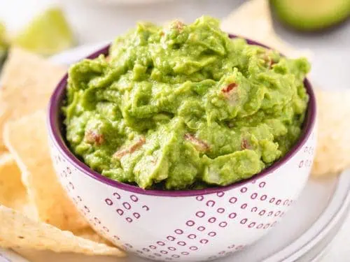 Close up view a bowl of dip next to chips.