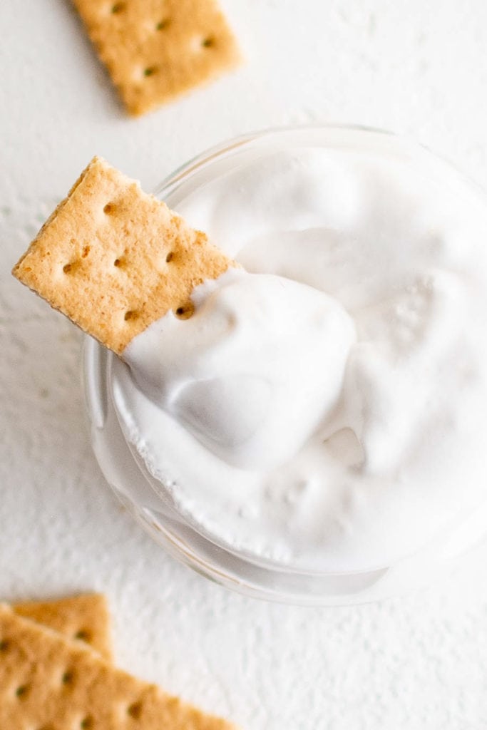Top down view of a graham cracker in a jar of marshmallow dessert.