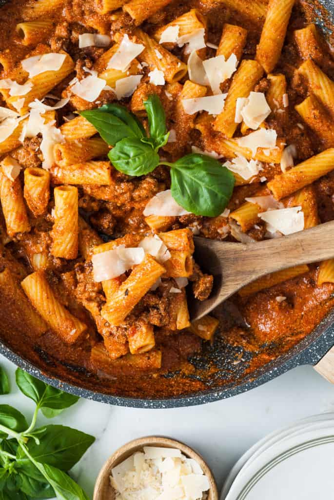 Close up view of a pan of pasta tossed in red sauce.