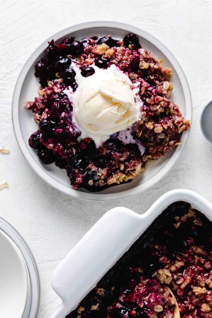 Close up view of berry crisp topped with vanilla ice cream on a plate.