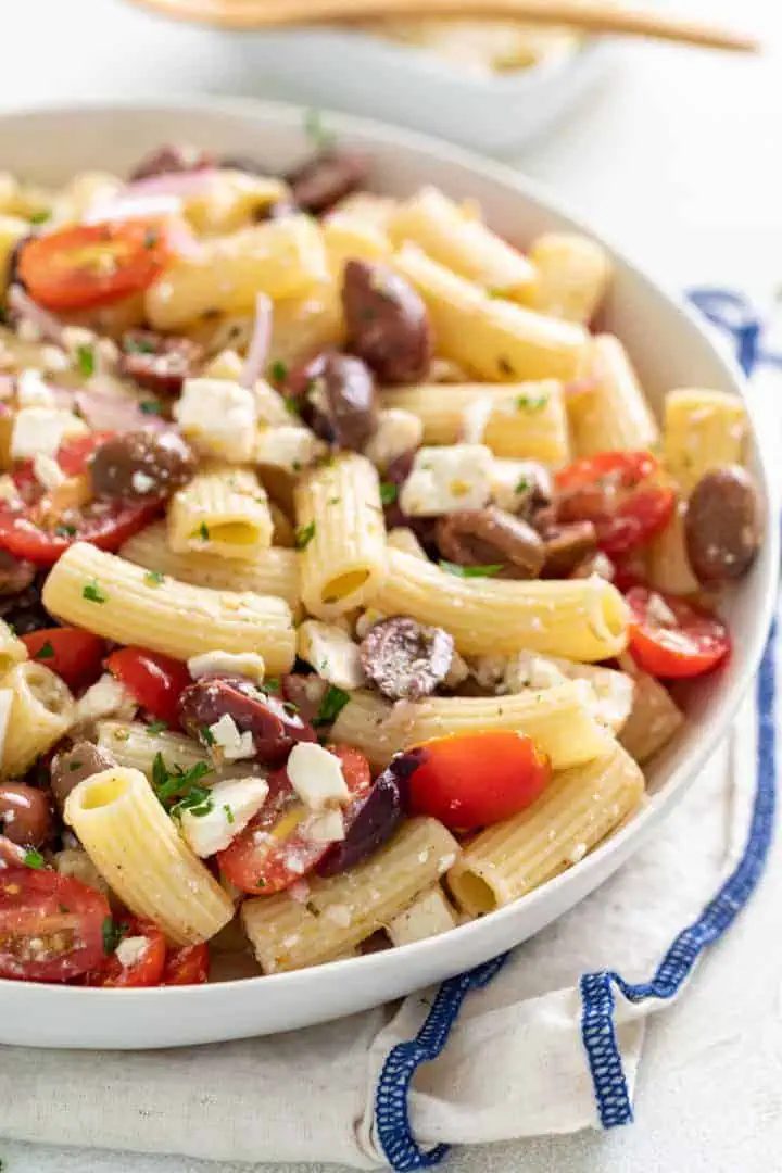 Olives, tomatoes, and feta in pasta salad in a dish.