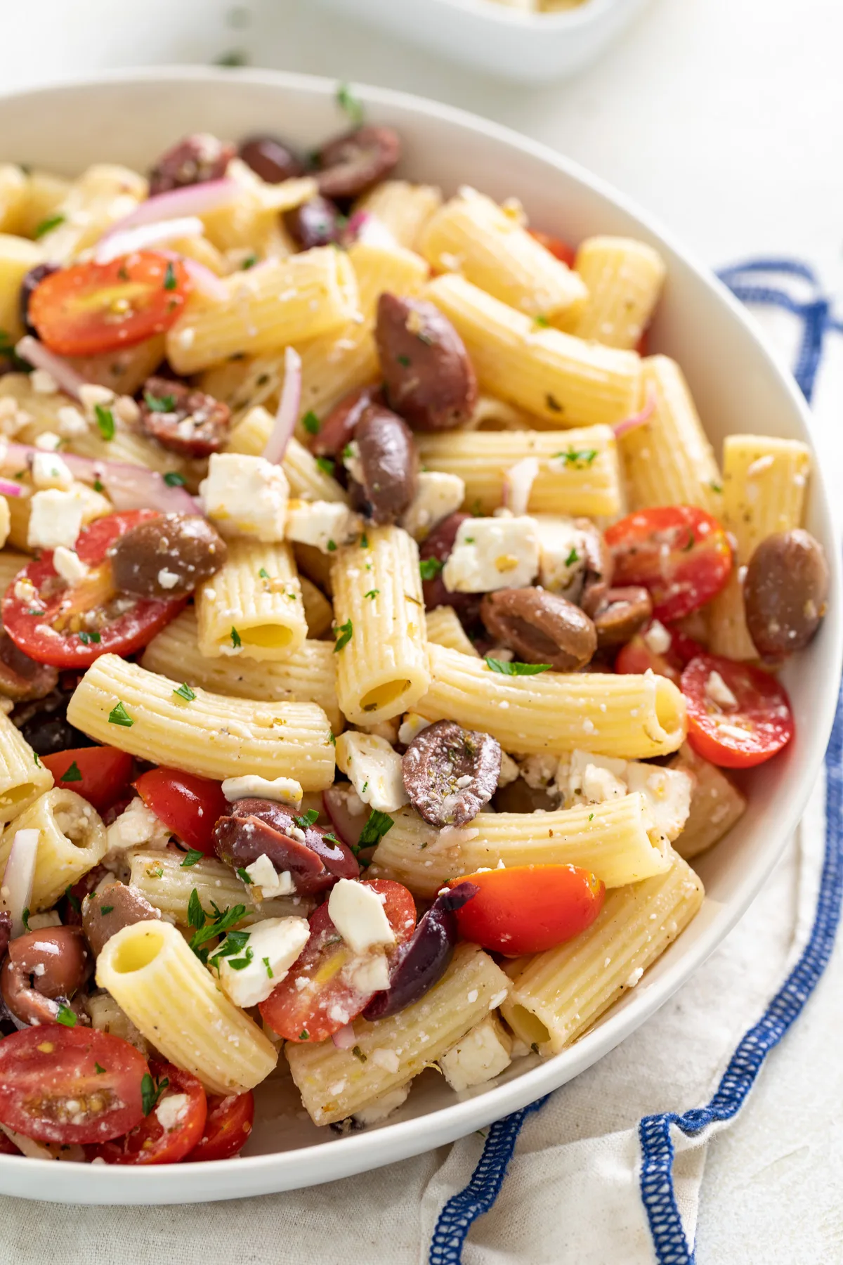 Side view of pasta salad with tomatoes and olives in a bowl.