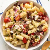 Top down view of a round serving dish filled with fresh greek pasta salad.