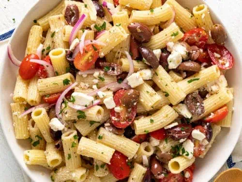 Top down view of a round serving dish filled with fresh greek pasta salad.