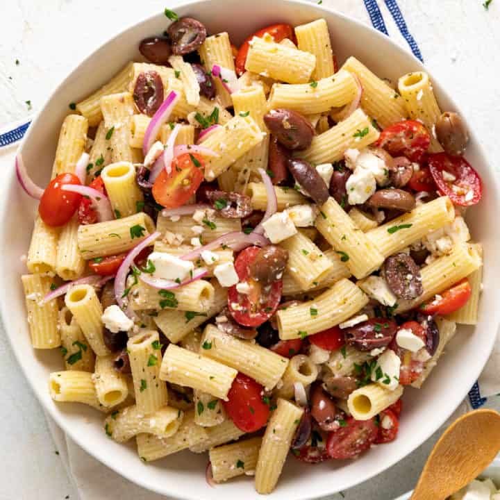 Top down view of a round serving dish filled with fresh greek pasta salad.