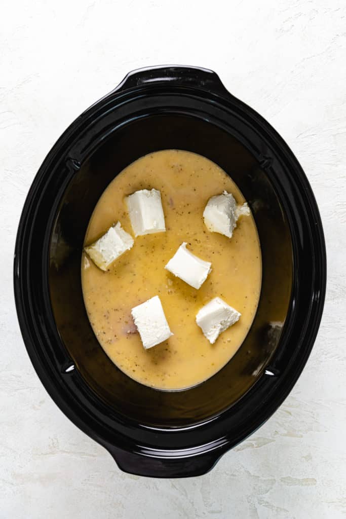 Cubed cream cheese placed on top of raw chicken and Italian chicken.