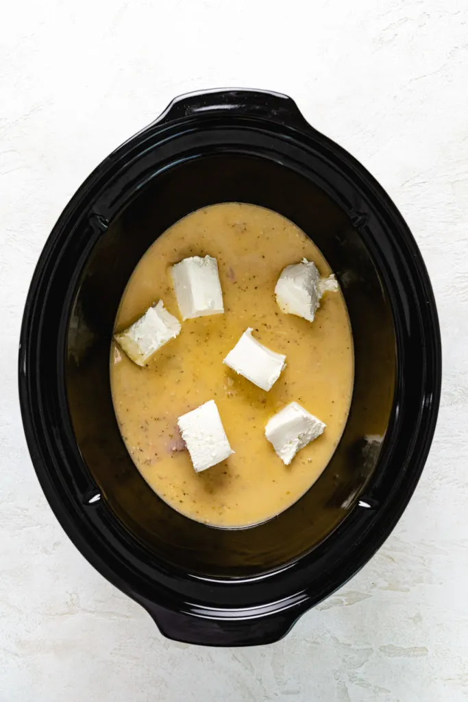 Cubed cream cheese placed on top of raw chicken and Italian chicken.