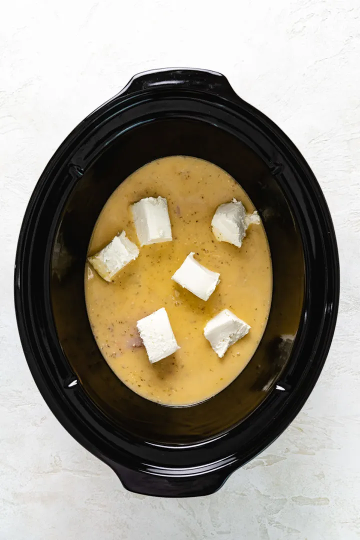 Slow Cooker Olive Garden Chicken Pasta Cubed cream cheese placed on top of raw chicken and italian chicken.