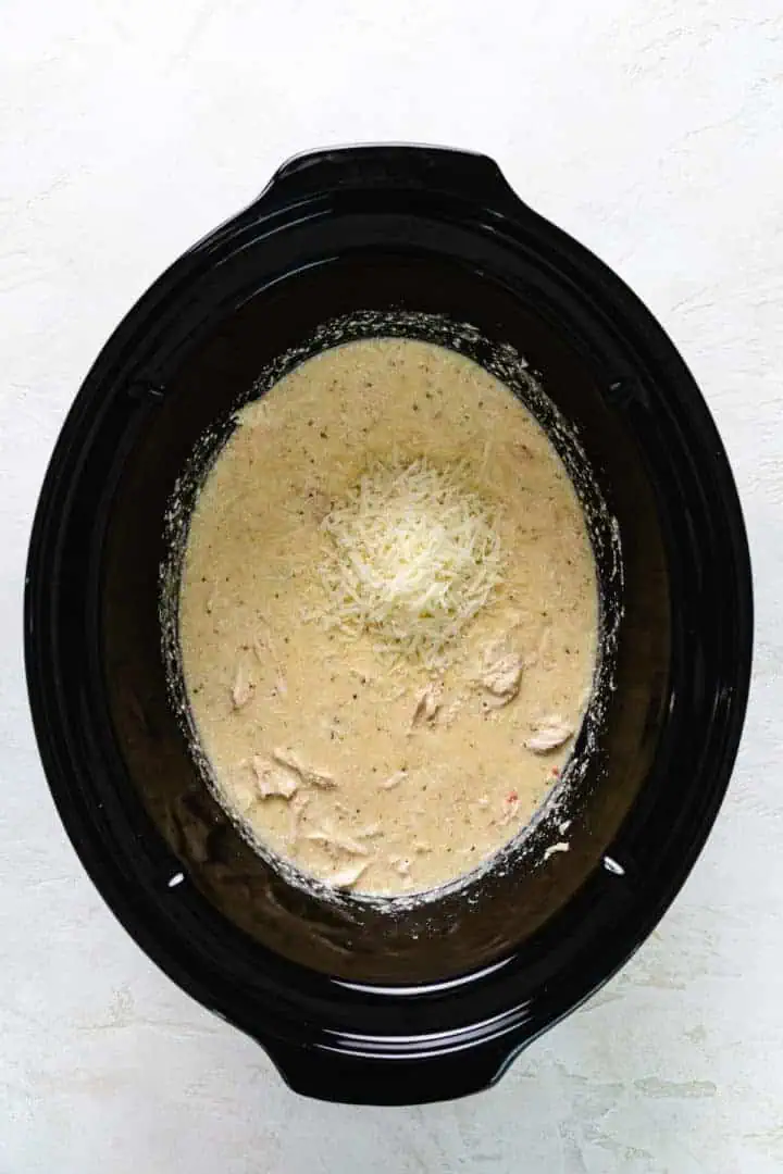 Slow Cooker Olive Garden Chicken Pasta Parmesan cheese added to a slow cooker filled with italian dressing, cream cheese, and chicken.