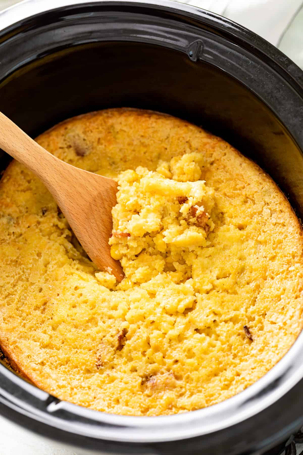 Wooden spoon scooping a helping of corn casserole.