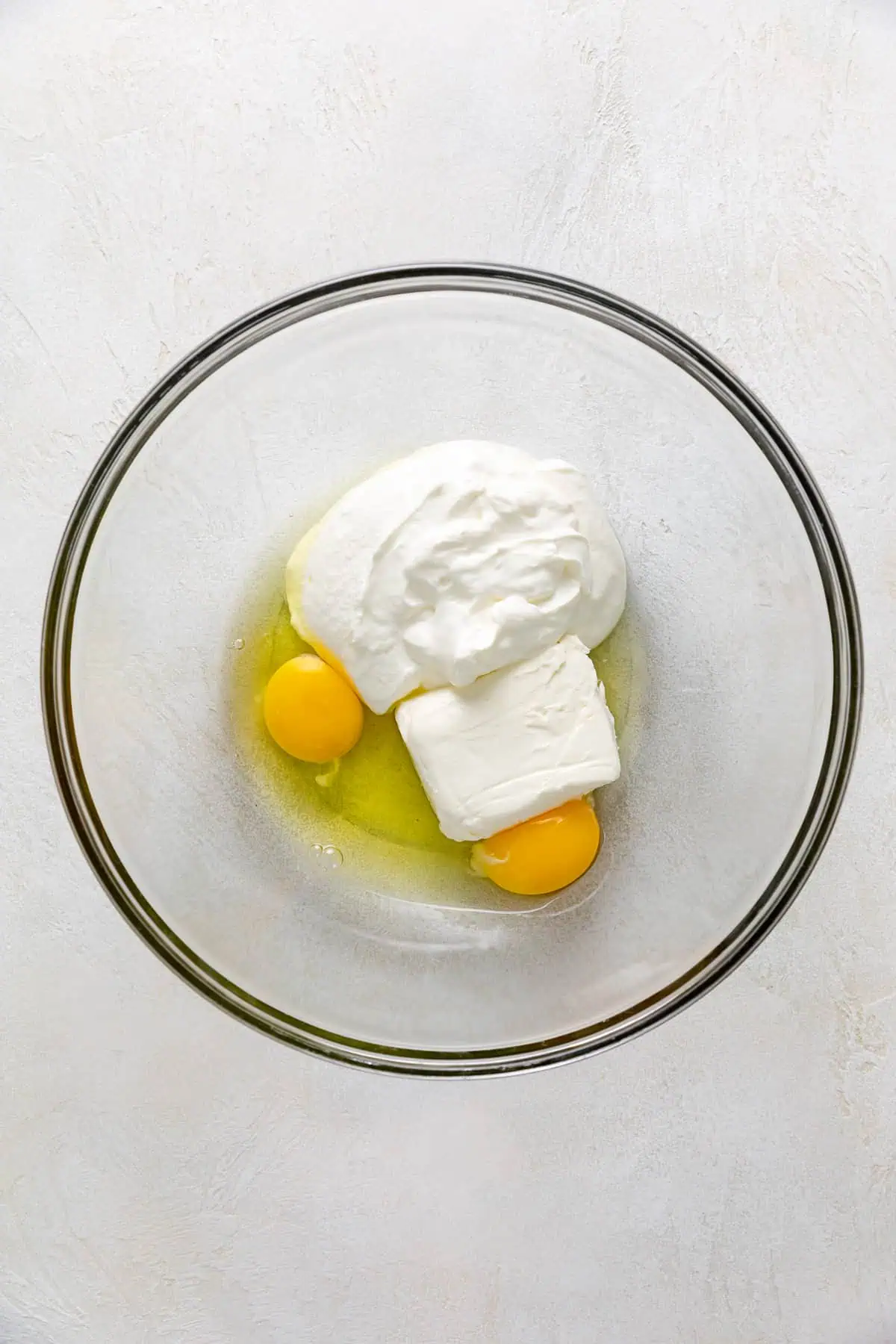 Eggs, sour cream, and cream cheese in a glass bowl.