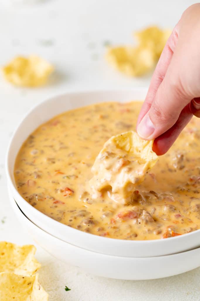 Hand holding a chip dipping cheese dip.