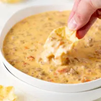 Chip dipping into a bowl of beef and sausage dip.