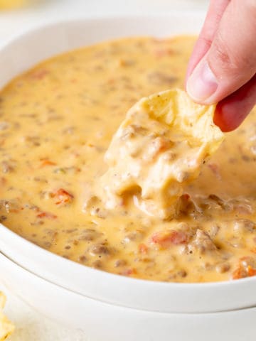 Chip dipping into a bowl of beef and sausage dip.