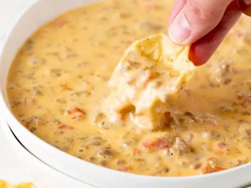 Chip dipping into a bowl of beef and sausage dip.