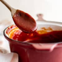 Spoon dipping into a pan of bbq sauce.