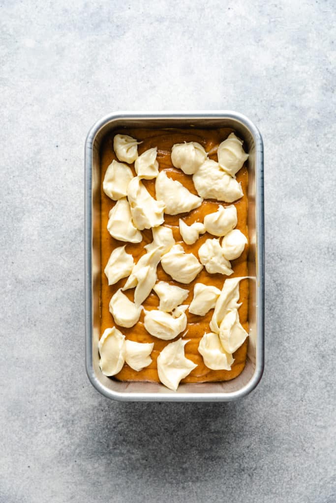 Cream cheese dotted over pumpkin bread batter.