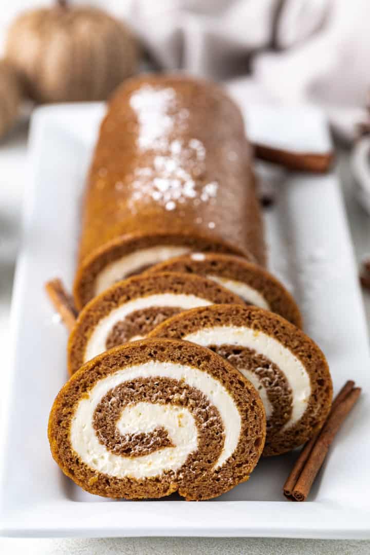 Front view of a cake roll with cream cheese filling on a white serving dish.