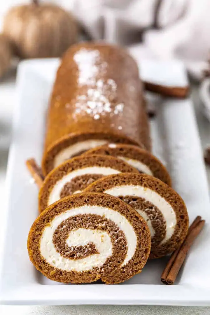 Front view of a cake roll with cream cheese filling on a white serving dish.