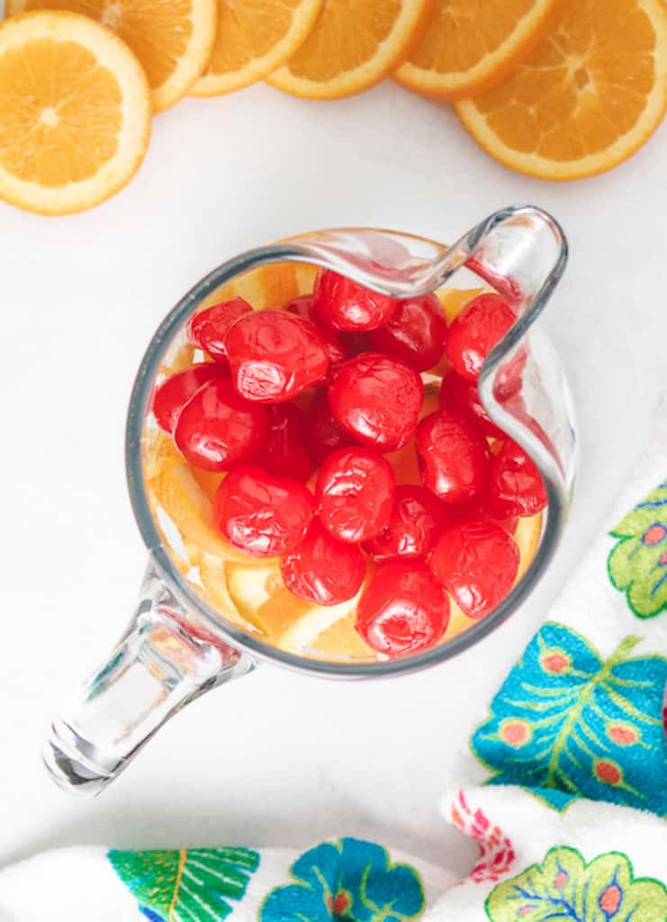 Close up view of cherries and orange slices in a pitcher.