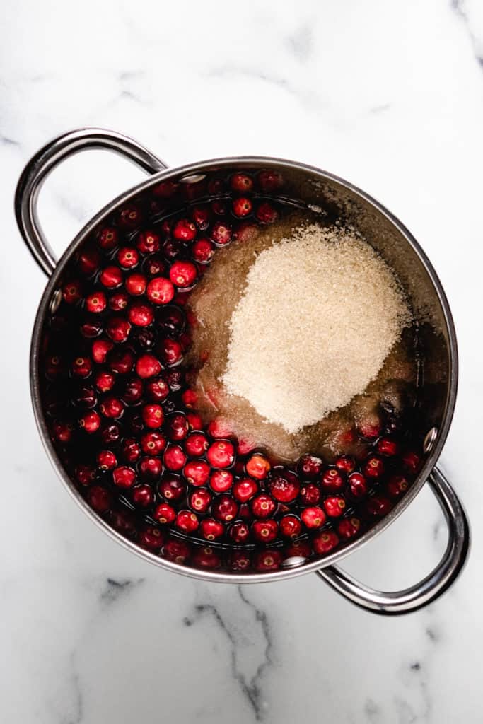 Top down view of sugar, water, and fresh cranberries in a pan.
