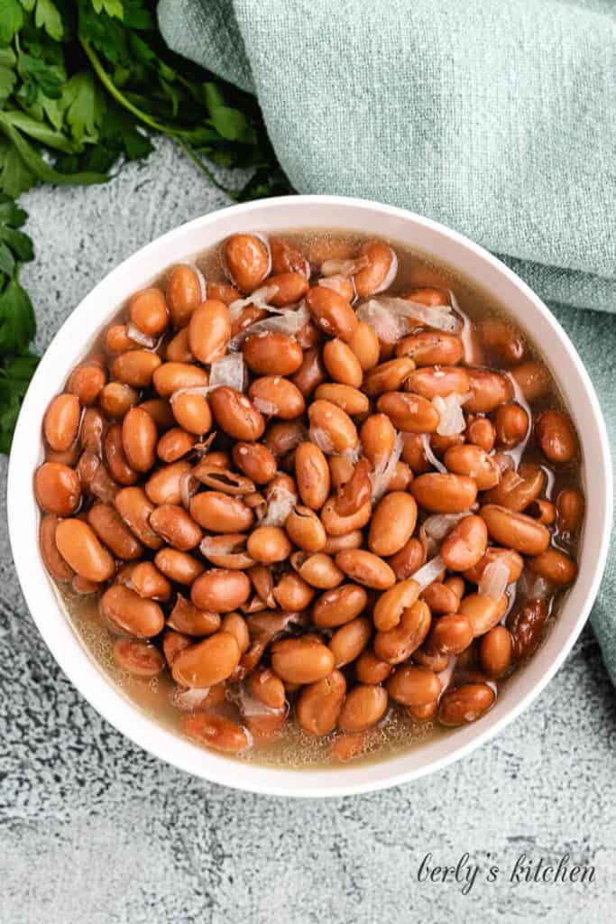 Top down view of a bowl of beans with ham and broth.