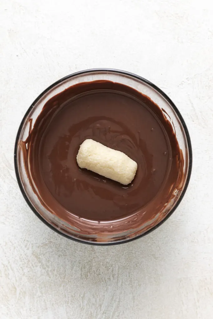 Coconut bar in a bowl of melted chocolate.