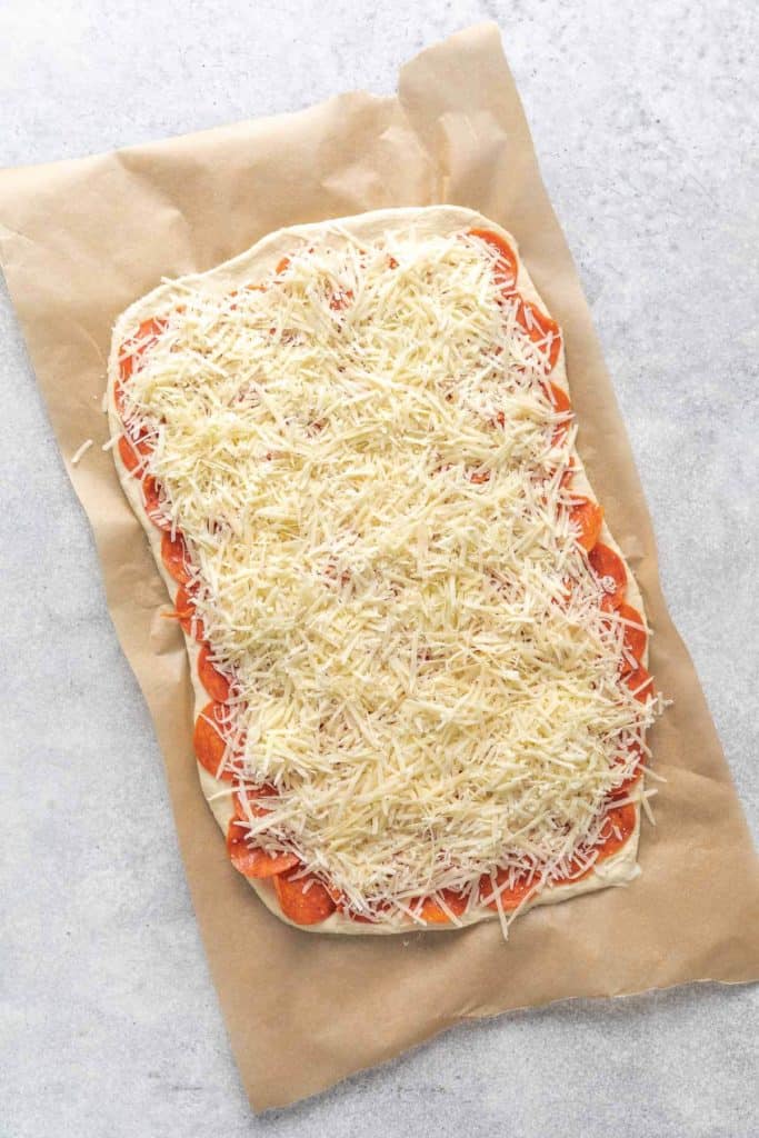 Pizza dough with pepperoni and shredded cheese on parchment paper.