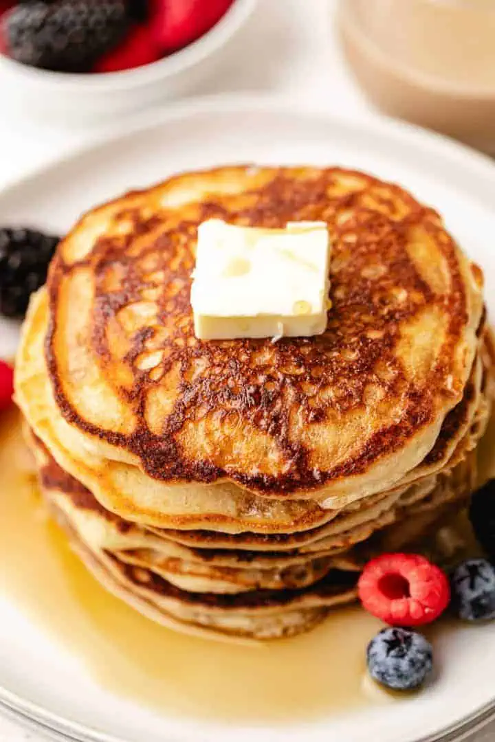 Close up view of maple syrup, pancakes and berries on a plate.