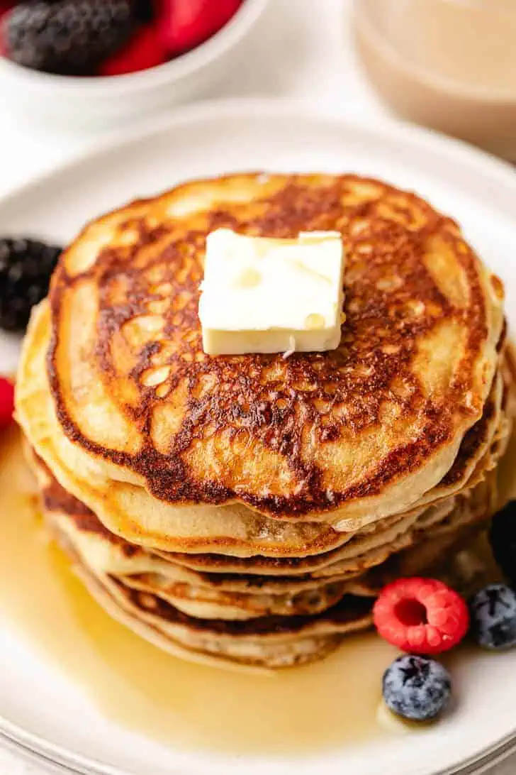 Close up view of maple syrup, pancakes and berries on a plate.