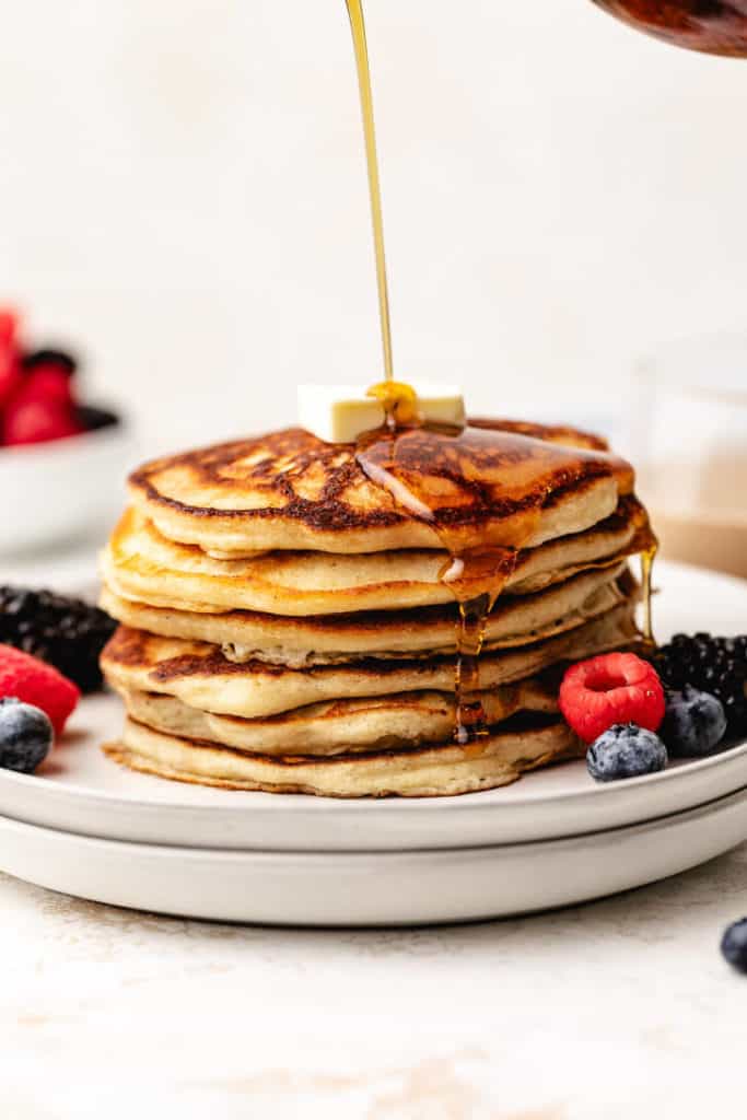 Maple syrup being poured over hot pancakes.