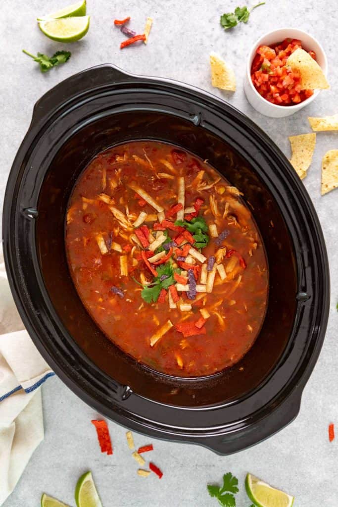 Top down view of a slow cooker filled with chicken tortilla soup.