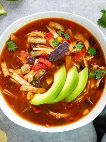 Close up view of a bowl of soup topped with sliced avocado.