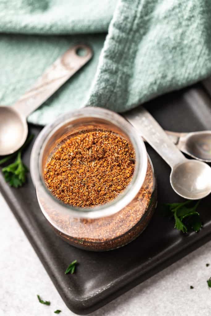 Jar of spices on a black colored board next to metal spoons.