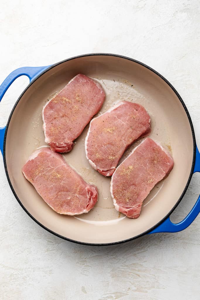 Seasoned pork chops in a pan.