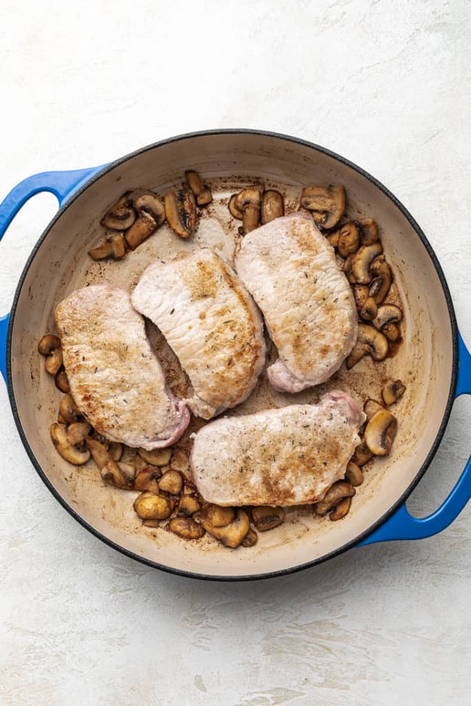 Pork chops and mushrooms in a pan.