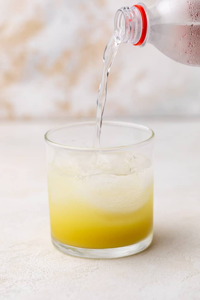 Club soda being added to a glass of ginger simple syrup.