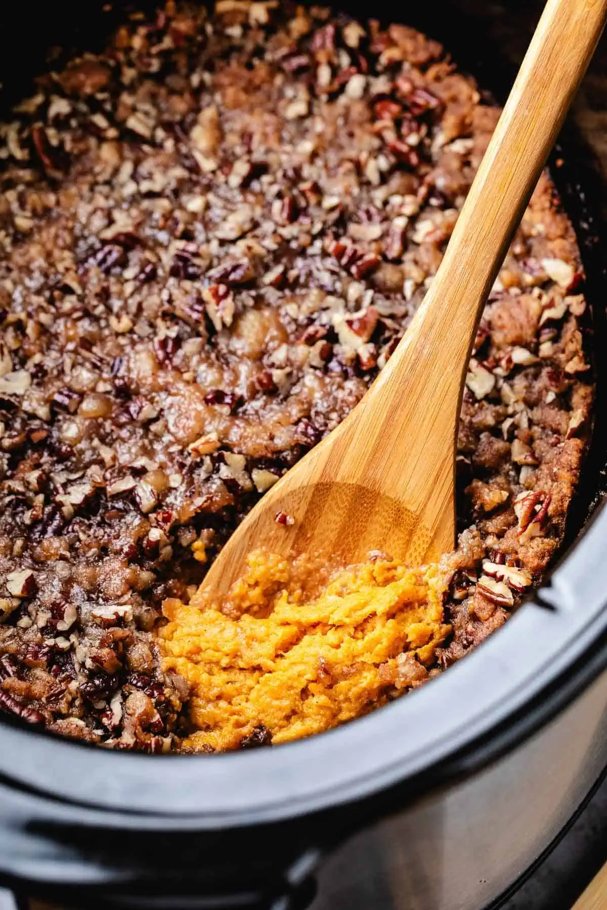Wooden spoon in a slow cooker filled with sweet potato casserole.