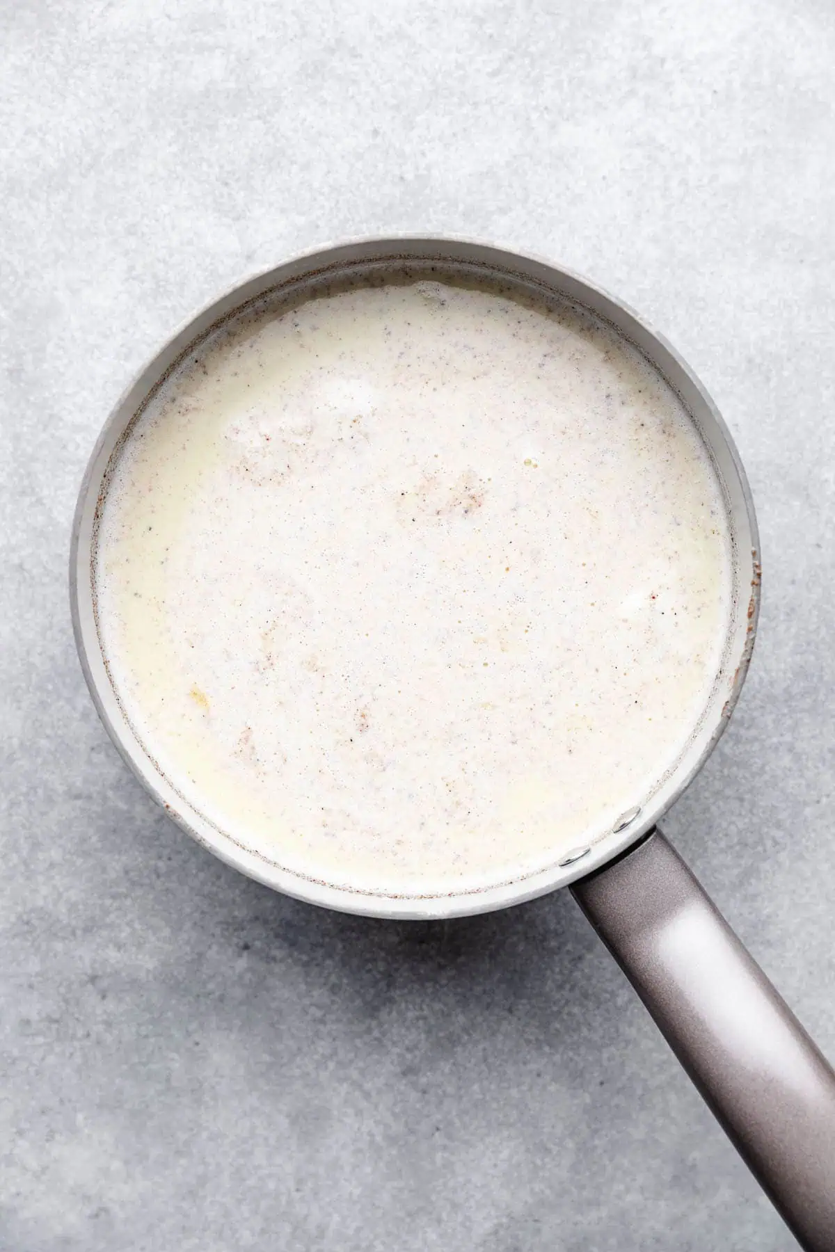 Heavy cream, milk, egg yolks, sugar, and nutmeg in a pan.