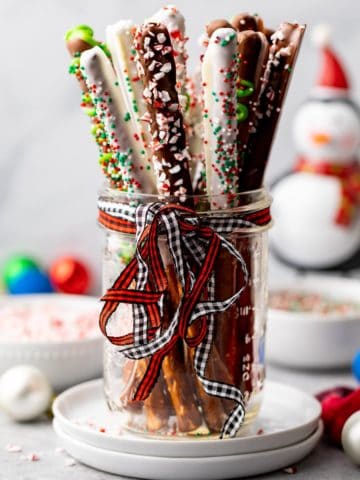 Mason jar with a ribbon filled with chocolate dipped pretzel rods.