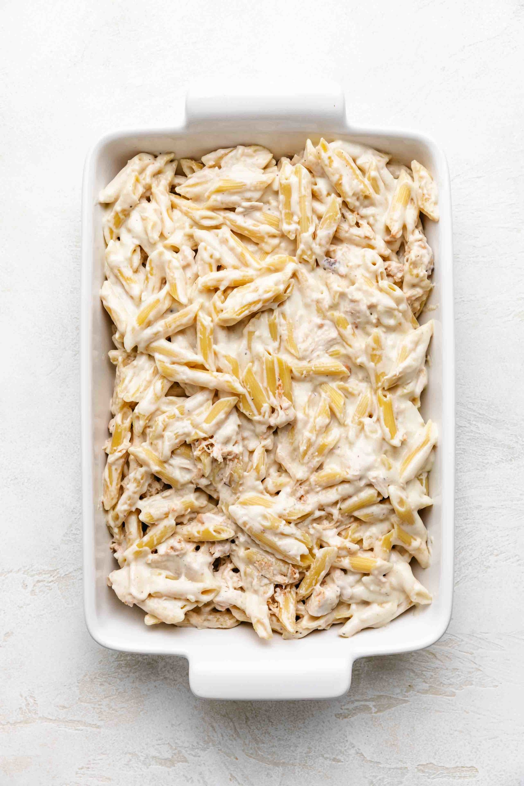 Pasta noodles, chicken and sauce in a baking dish.