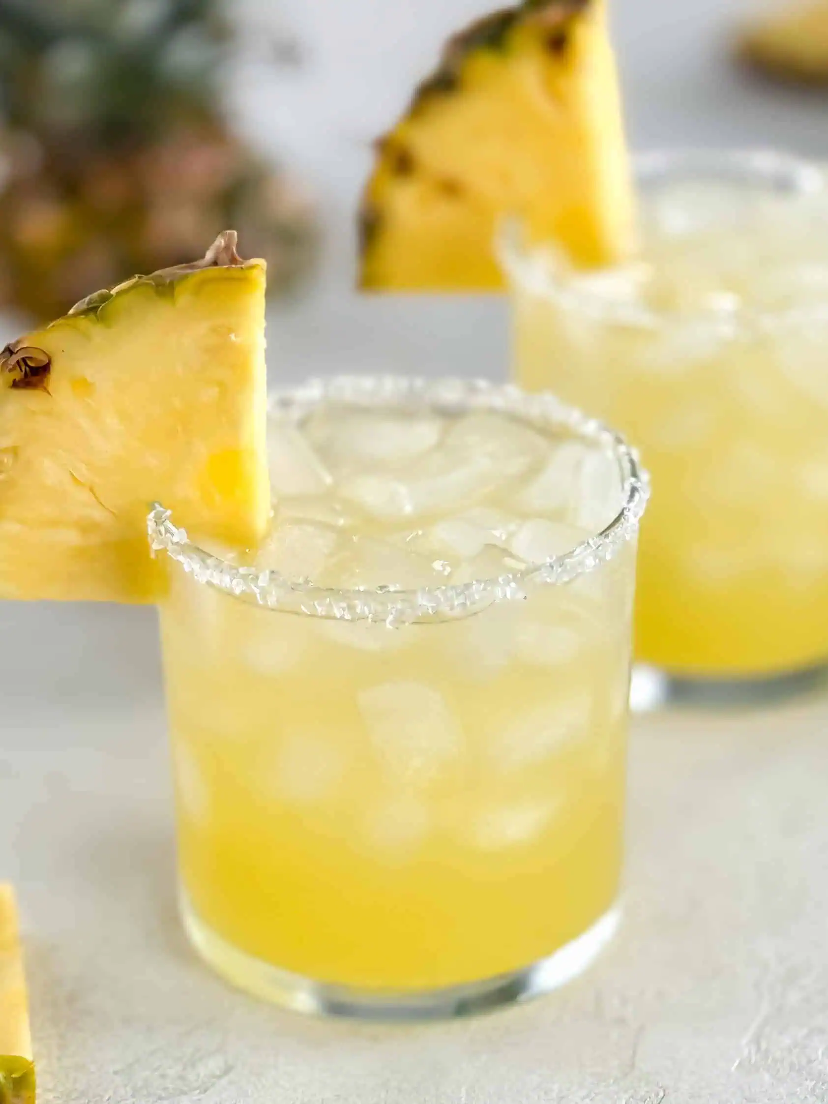 Close-up view of a chilled cocktail with ice and a slice of fresh pineapple on the rim.