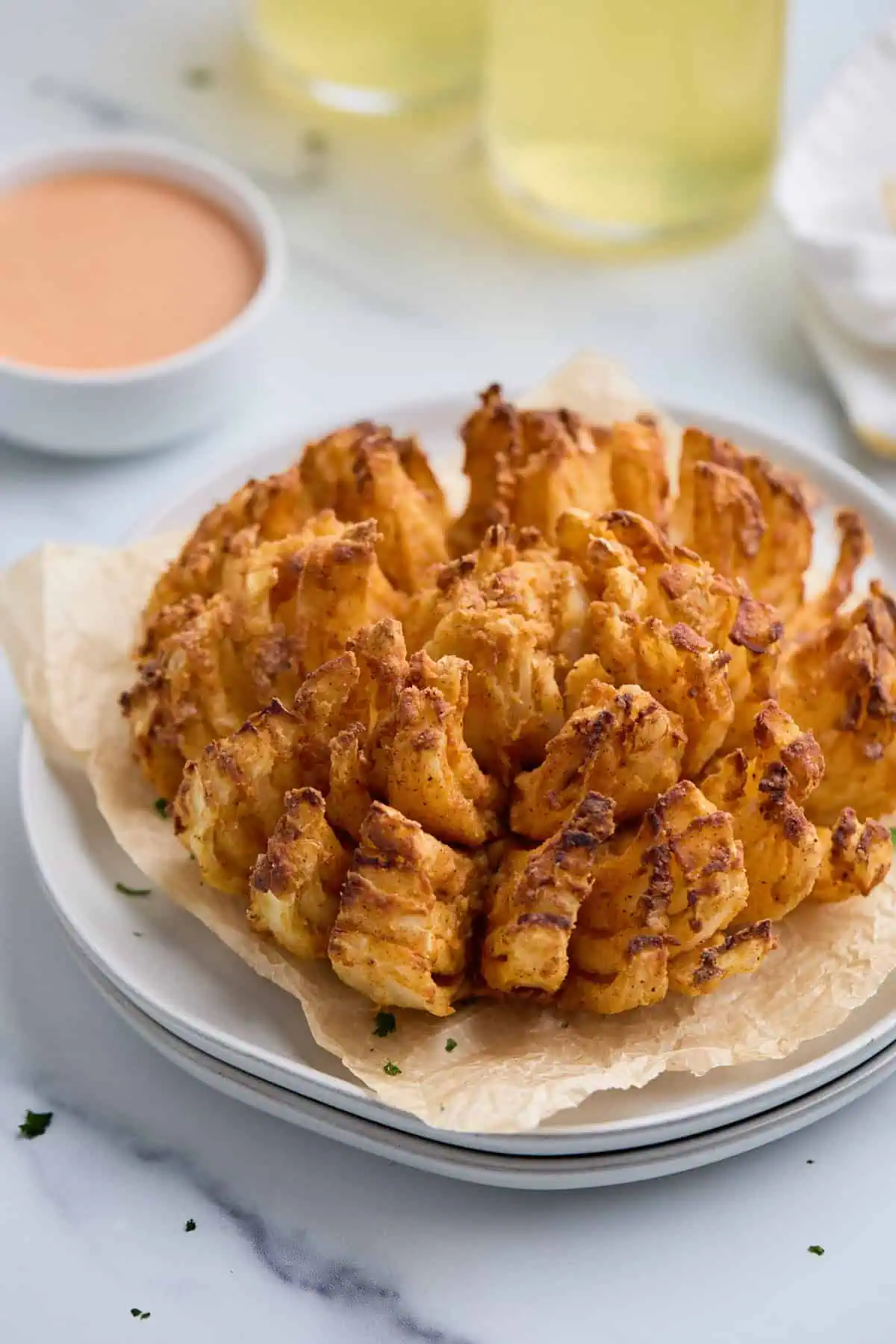 Air fryer blooming onion served on a white plate, garnished with parsley.