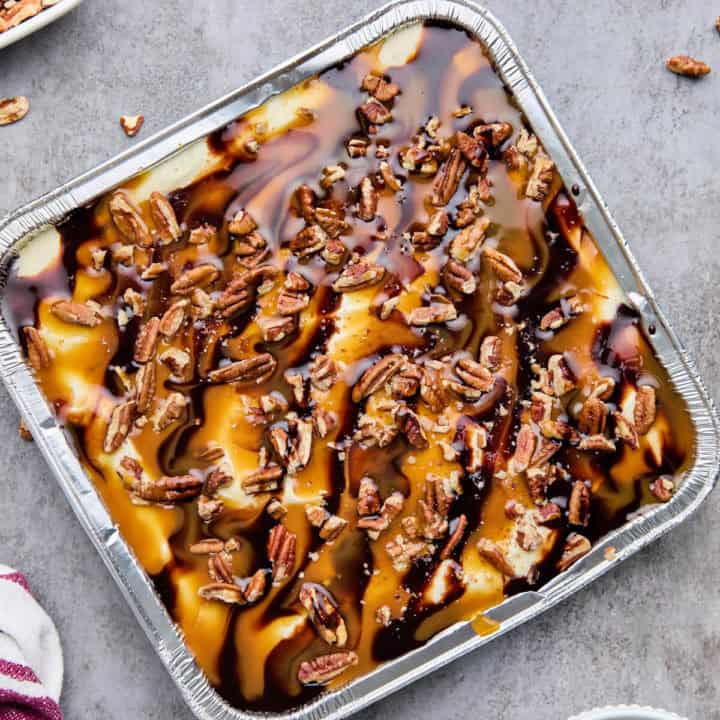 Top view of Turtle Cheesecake in an 8x8-inch pan with caramel and chocolate drizzles and chopped pecans.